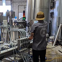 Danielle with her back turned toward the canning line at Device Brewing