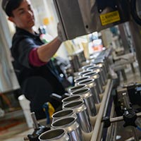 Cans on the conveyor with Lindsey blurred out and operating the canning line